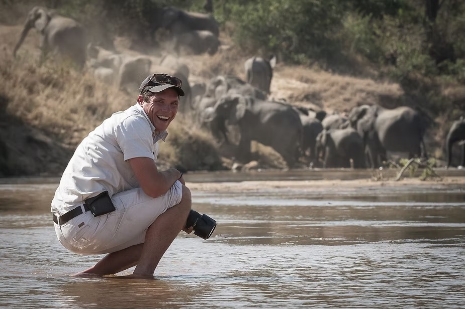 Crouching in the shallows to photograph an elephant herd crossing behind