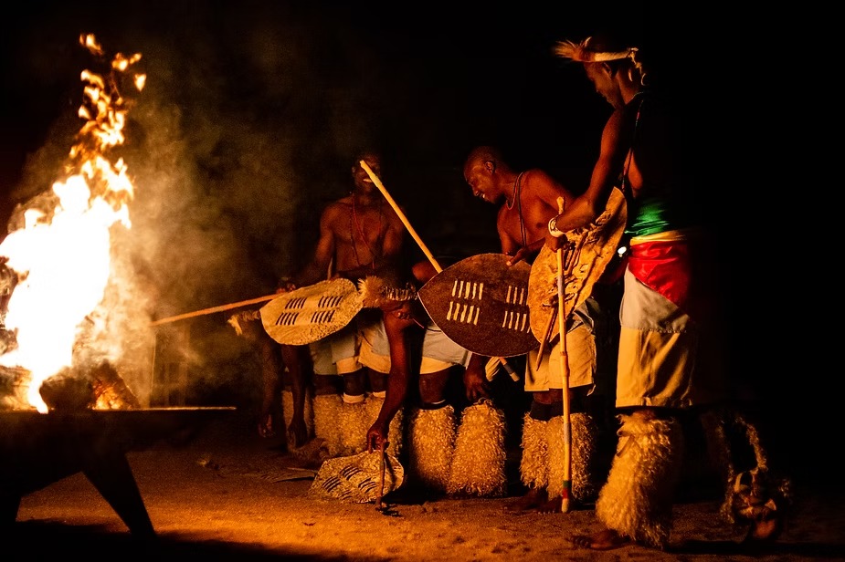 Dancers with shields and spears performing around a fire at night