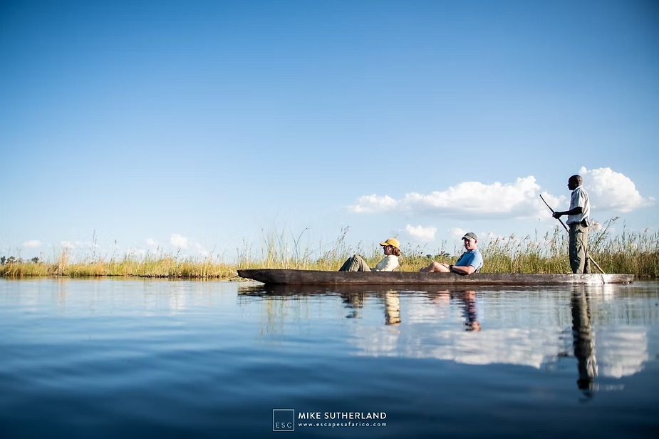 A poler guiding a mokoro across still water in the Okavango Delta