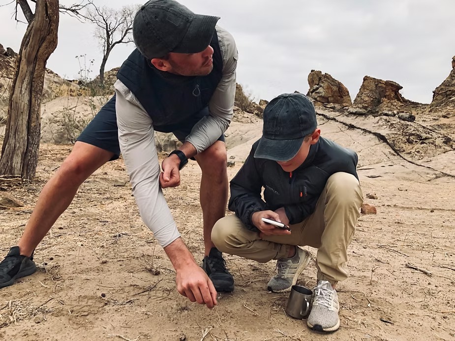 A guide and a young guest crouching over tracks in the sand