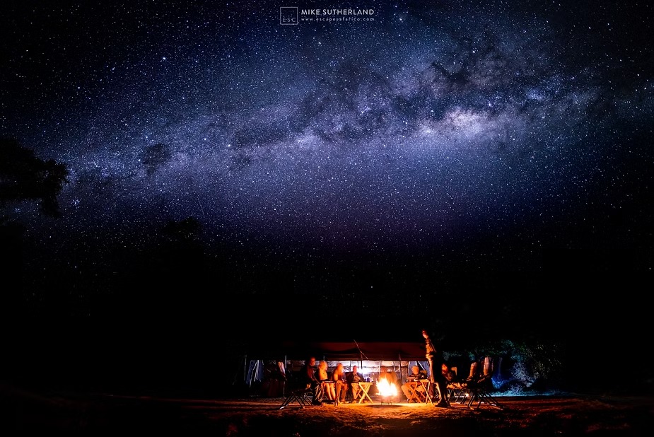 The Milky Way arching over a lantern-lit safari camp