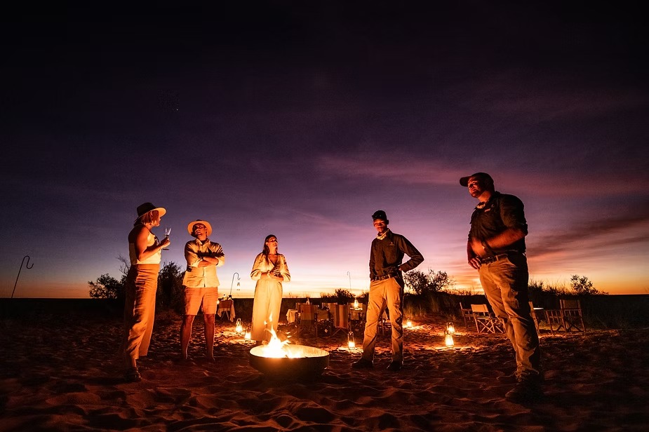 Guests gathered around a fire on the red Kalahari sand at Tswalu