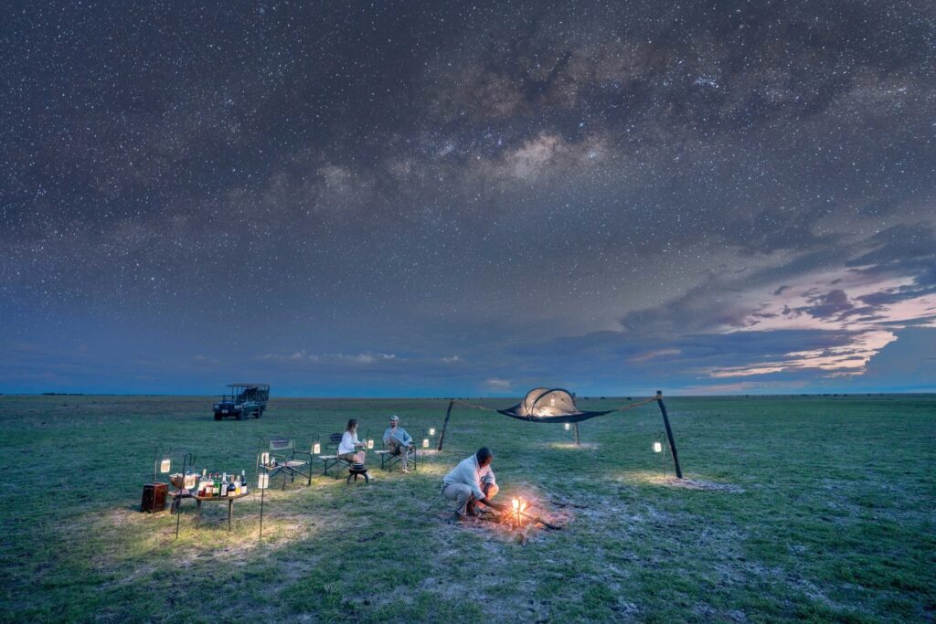 Bedrolls and a fire beneath the Milky Way on the plains at Time and Tide Liuwa Plains